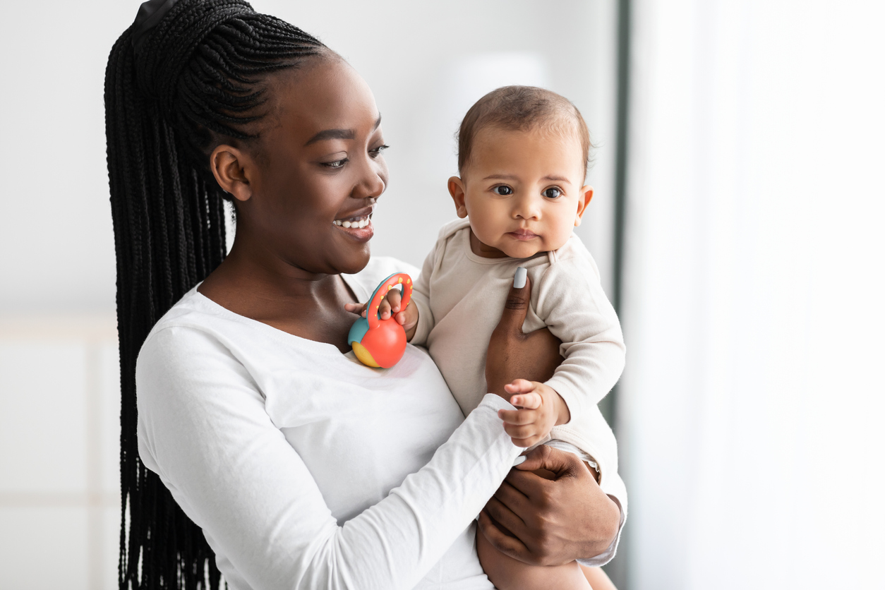 african american mom hugging her cute infant playing with toy
